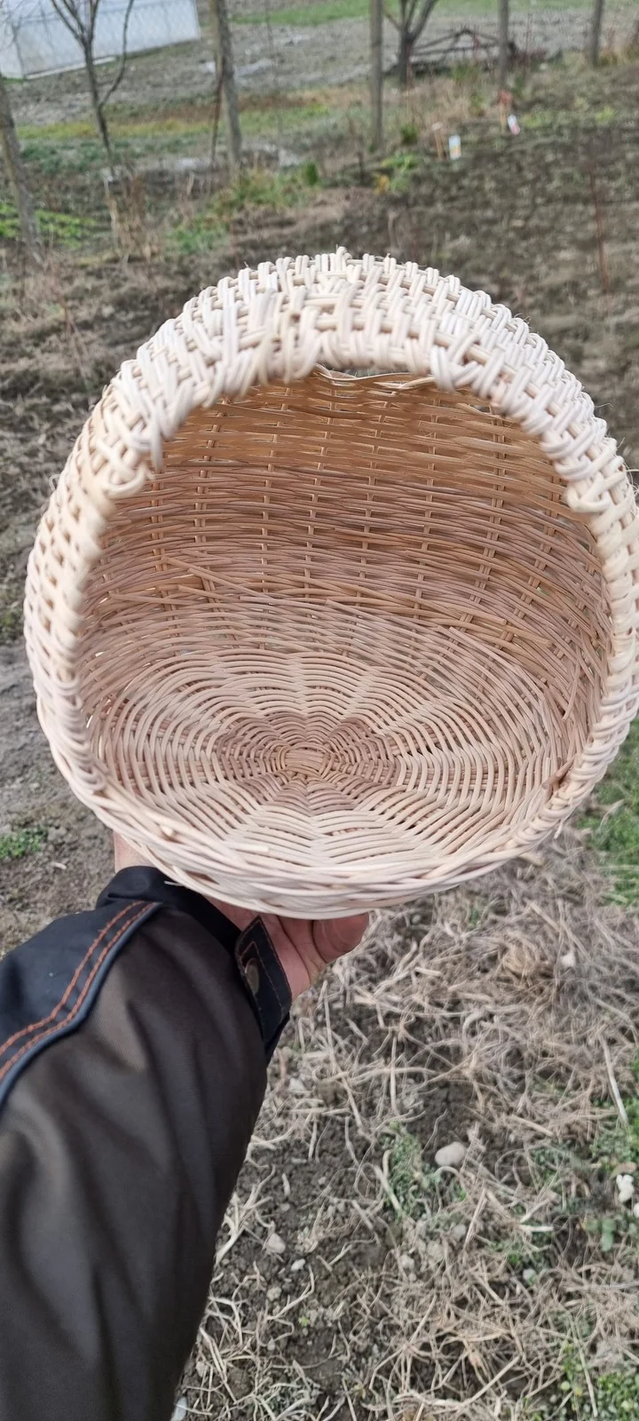 A light-coloured woven nesting basket for hens, held in a hand.